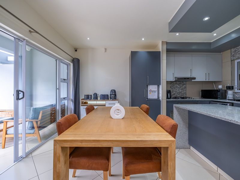 Modern open-plan kitchen and dining area featuring granite countertops, sleek cabinetry, recessed lighting, and large sliding doors leading to a private patio.