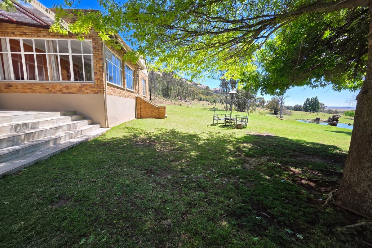 A view of the rear brick facade of the farmhouse, featuring tiled steps leading to the garden with mature trees and open landscape.