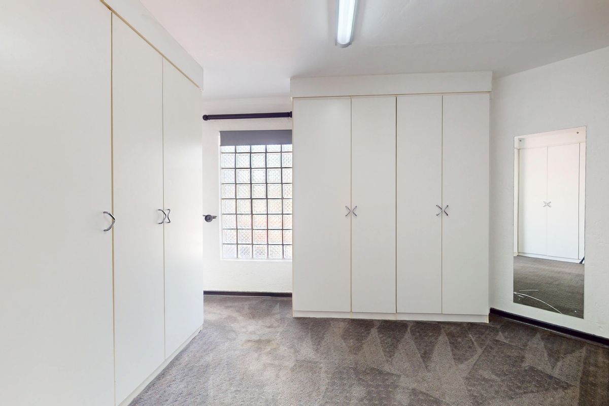 A bedroom featuring extensive built-in cupboard storage, a unique glass block window, and neutral carpeting.