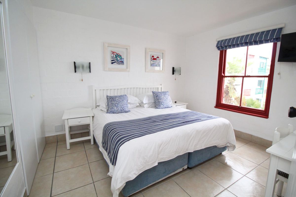A bright bedroom featuring tiled flooring, painted brick walls, and a sash window with a red frame.