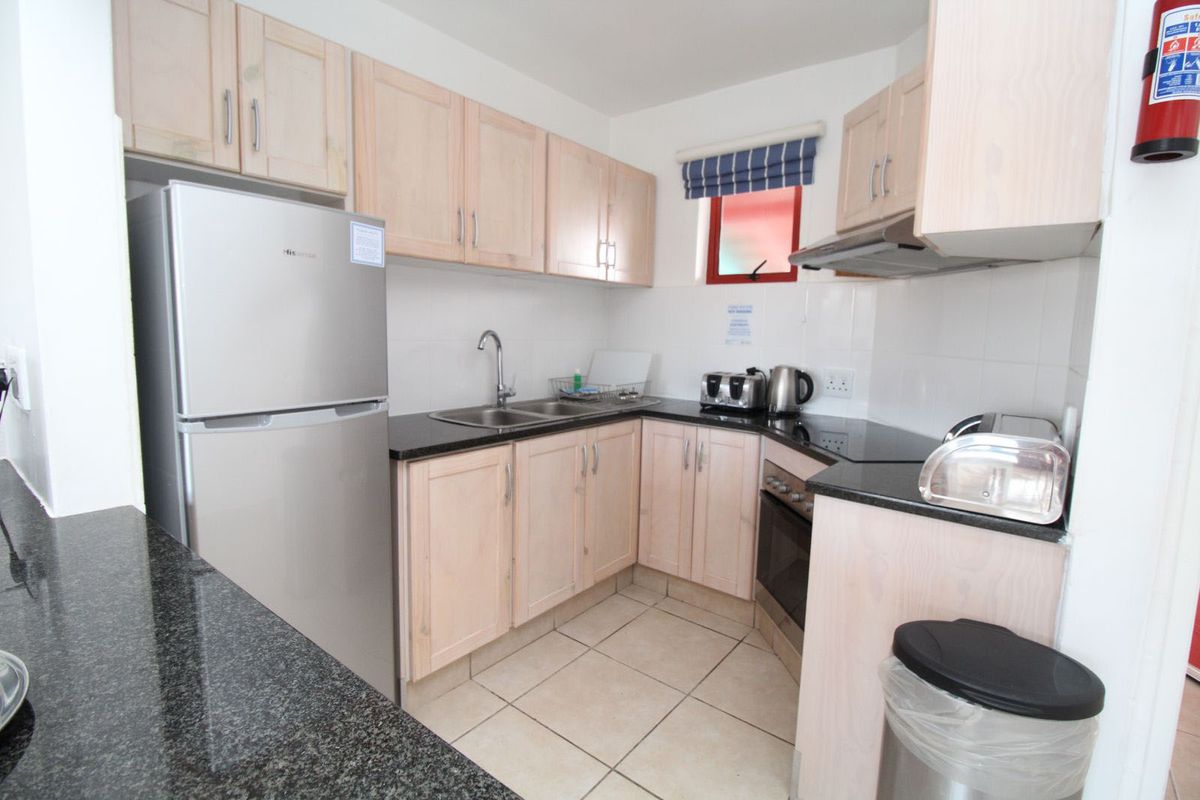 Compact kitchen featuring light wood cabinetry, dark granite countertops, a double sink, and built-in oven with extractor fan.