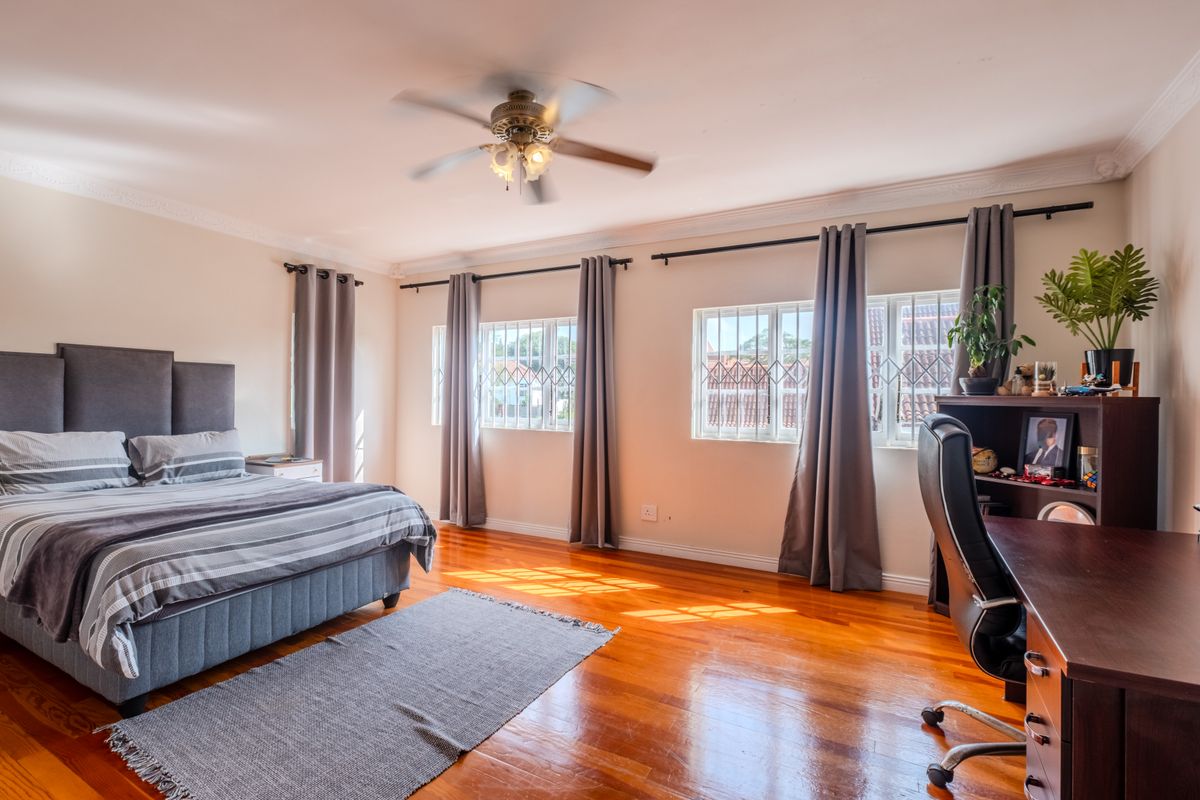 Spacious bedroom featuring polished hardwood flooring, crown molding, a ceiling fan, and large windows fitted with security bars.