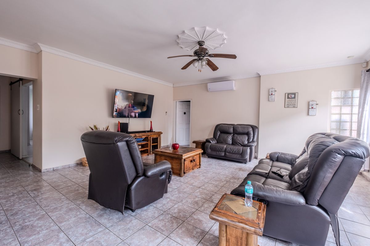 A spacious living room featuring tiled flooring, a ceiling fan with decorative rose, and a wall-mounted air conditioning unit.