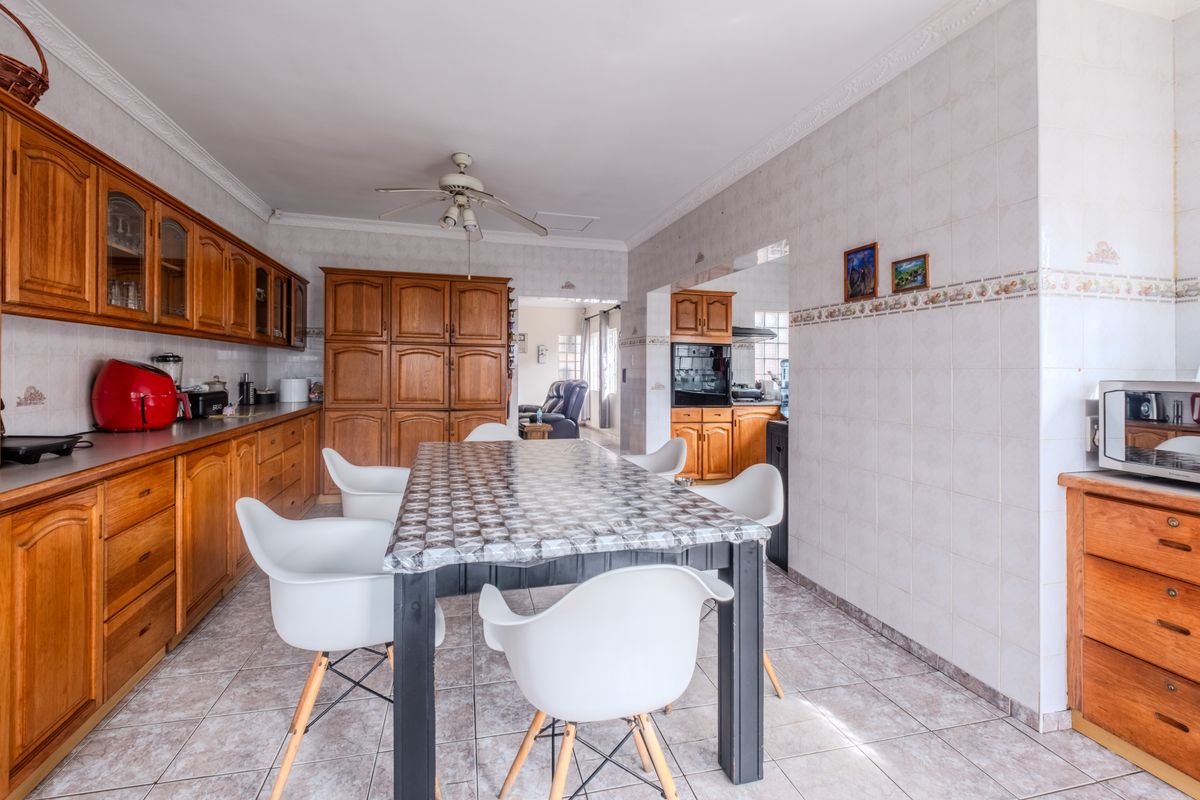 Spacious kitchen featuring extensive wooden cabinetry, tiled walls and flooring, and a central dining area, offering a functional layout with classic finishes.