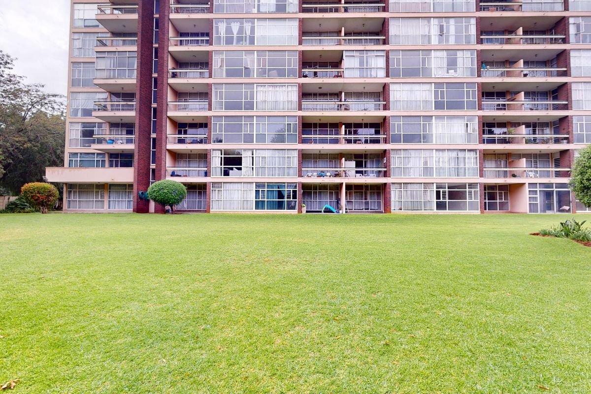 Rear view of a multi-story apartment building featuring private balconies with sliding glass doors overlooking a large, well-maintained communal lawn.