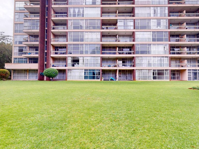 Rear view of a multi-story apartment building featuring private balconies with sliding glass doors overlooking a large, well-maintained communal lawn.