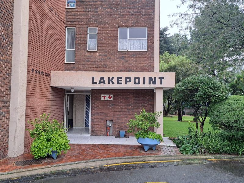 Front entrance view of Lakepoint apartment complex featuring a brick facade, paved walkway, and established garden surroundings.