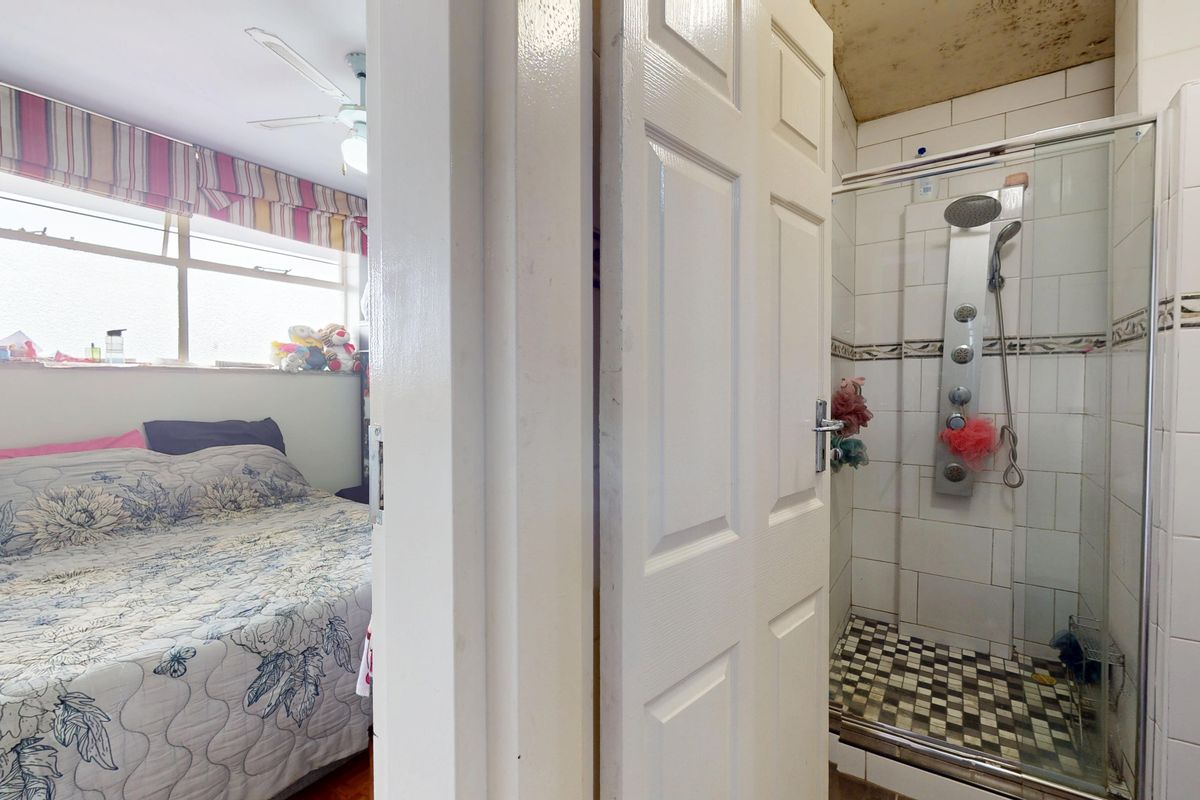 A bedroom featuring an en-suite shower room with a modern shower panel, though the ceiling shows signs of water damage.