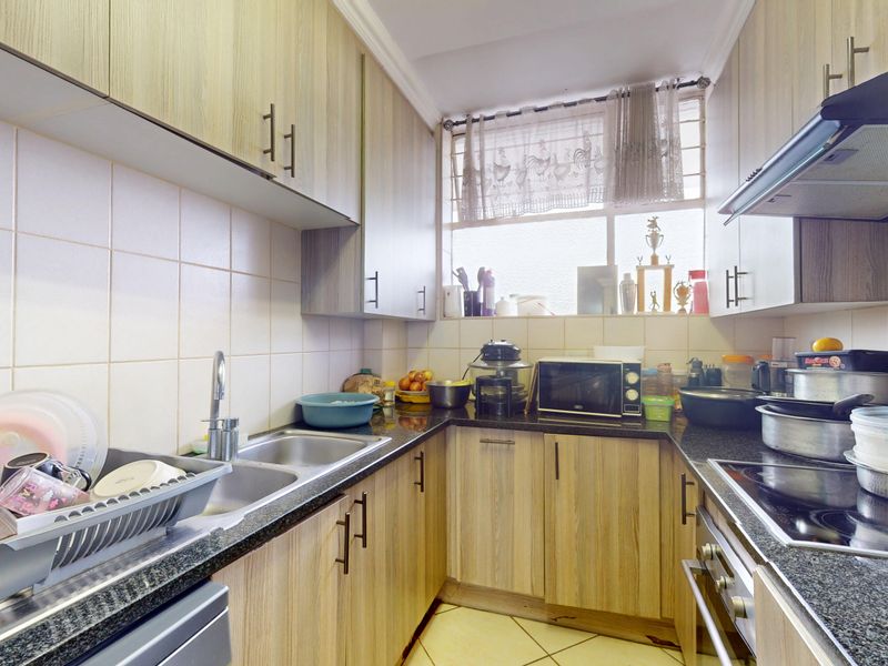 Compact galley-style kitchen featuring wood-look laminate cabinetry, granite countertops, tiled backsplash, and integrated cooking appliances.