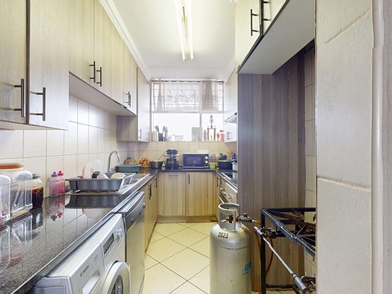 A functional galley-style kitchen featuring built-in cabinetry, granite countertops, tiled backsplash, and integrated space for laundry appliances.