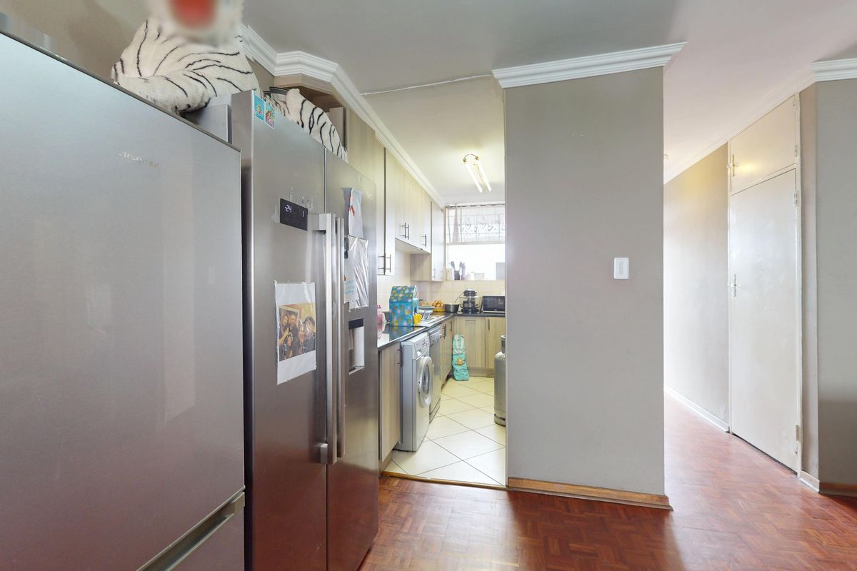 A functional kitchen featuring built-in cabinetry, laminate countertops, and tiled flooring, with an adjacent hallway area finished in parquet flooring.
