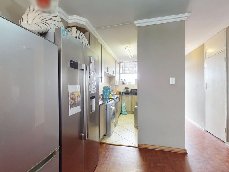 A functional kitchen featuring built-in cabinetry, laminate countertops, and tiled flooring, with an adjacent hallway area finished in parquet flooring.