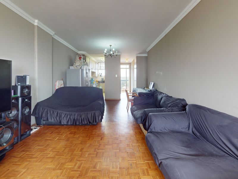 Open plan living area featuring parquet flooring and crown molding, leading through to a kitchen and balcony access.