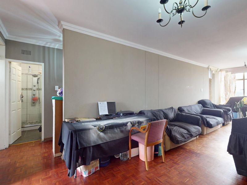 Spacious living area featuring classic parquet flooring, crown molding, and a chandelier, with an adjacent bathroom visible through the doorway.