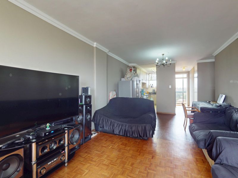 Open-plan living and dining area featuring parquet flooring, crown molding, and a connected kitchen space with access to a balcony.