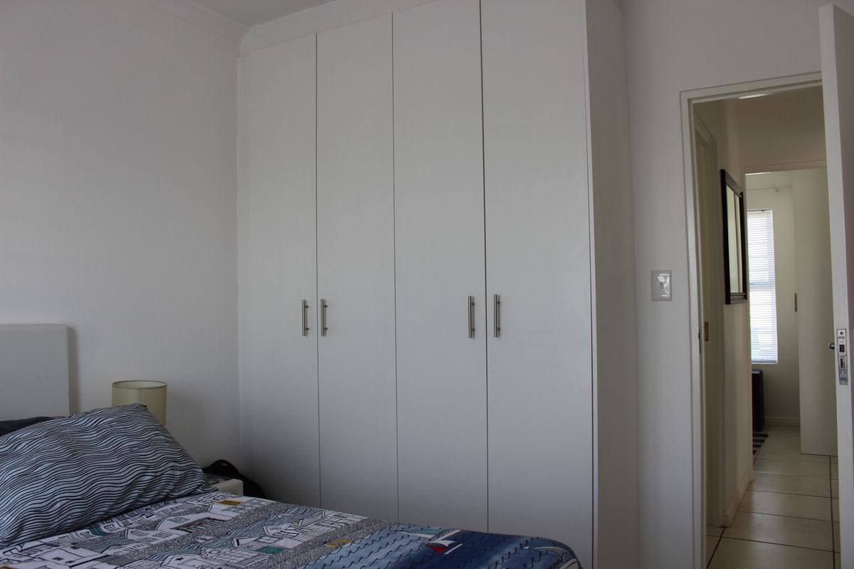 A bedroom featuring a clean, white built-in wardrobe with modern handles and coving detail, leading into an adjacent hallway.