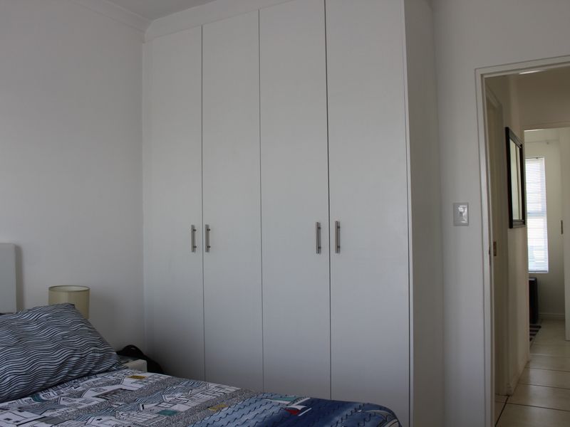 A bedroom featuring a clean, white built-in wardrobe with modern handles and coving detail, leading into an adjacent hallway.