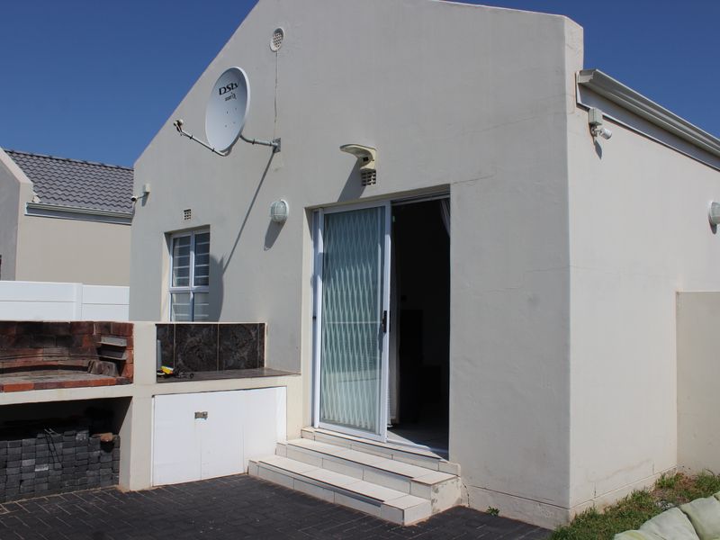 Rear exterior view of the townhouse featuring a paved patio area with a built-in brick braai and sliding door access.