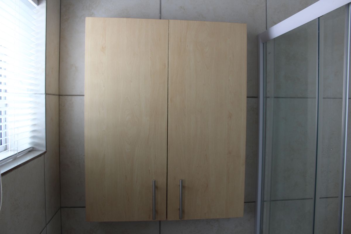 A bathroom featuring a wall-mounted light wood vanity cabinet, tiled walls, and a glass shower enclosure.