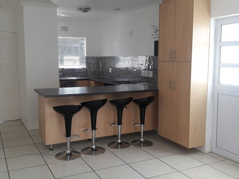 A functional kitchen featuring light wood cabinetry, a breakfast bar, tiled backsplash, and tiled flooring, offering a practical layout for daily use.