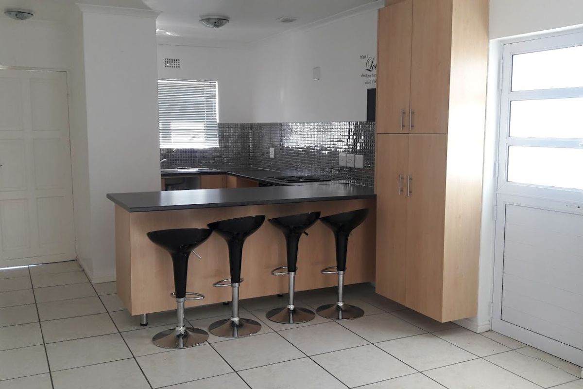 A functional kitchen featuring light wood cabinetry, a breakfast bar, tiled backsplash, and tiled flooring, offering a practical layout for daily use.