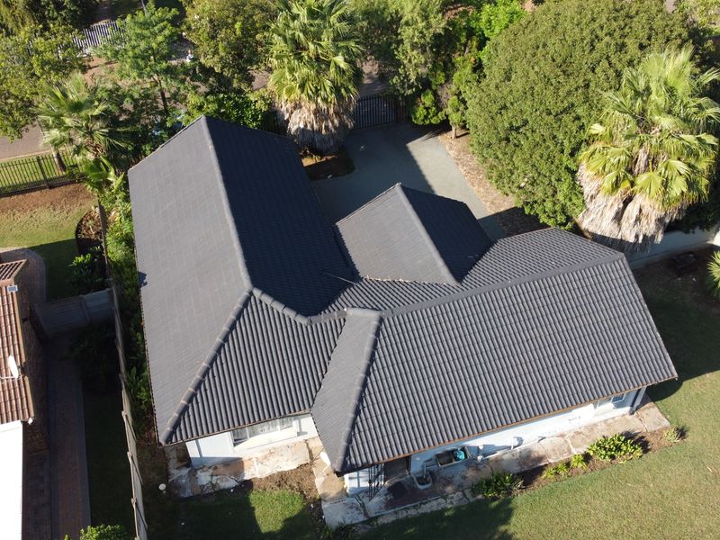 Aerial view of the property showcasing the dark tiled roof, paved driveway, and surrounding garden area.