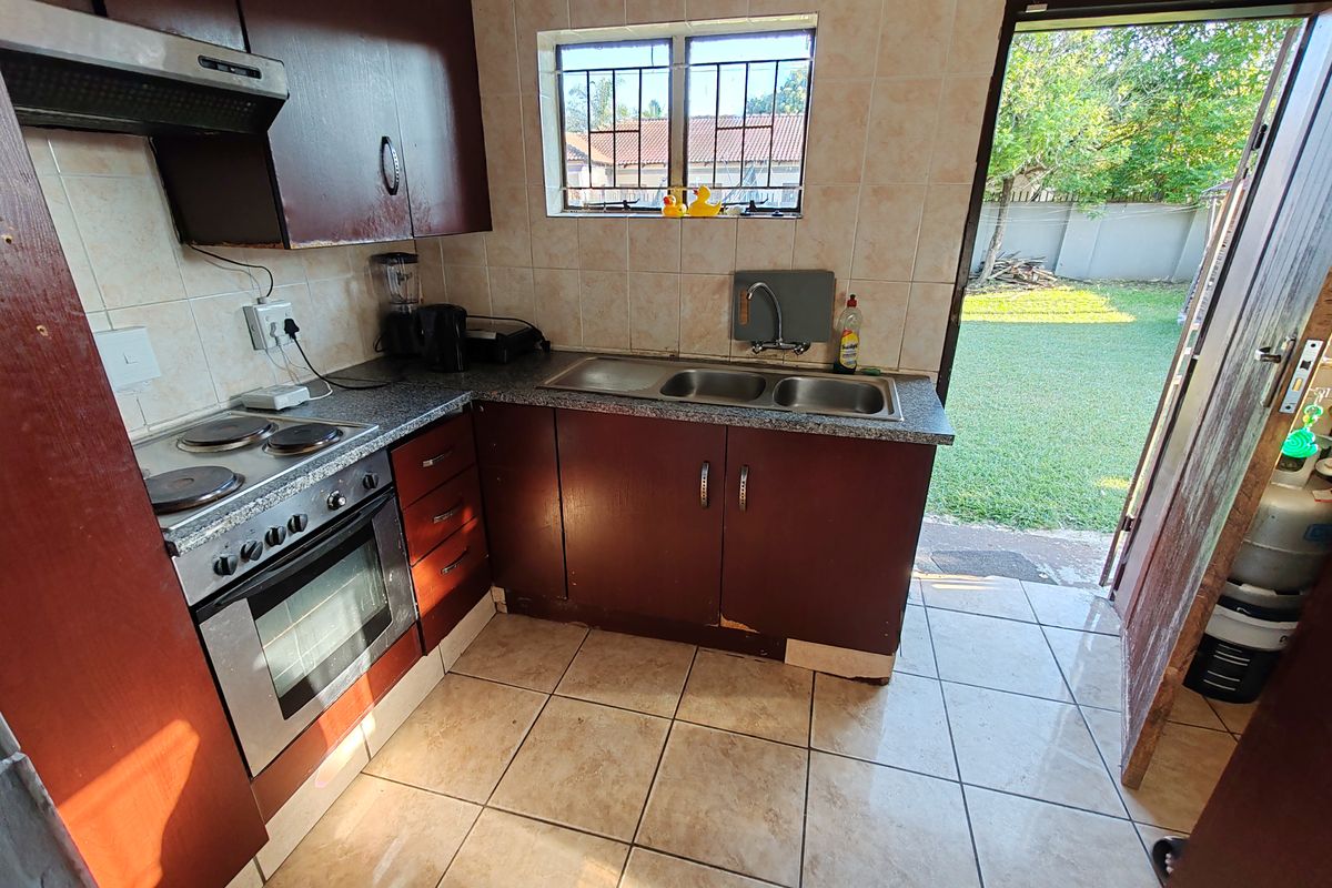 A compact kitchen featuring dark wood cabinetry, a double bowl sink, and an electric stove, with direct access to the rear garden.