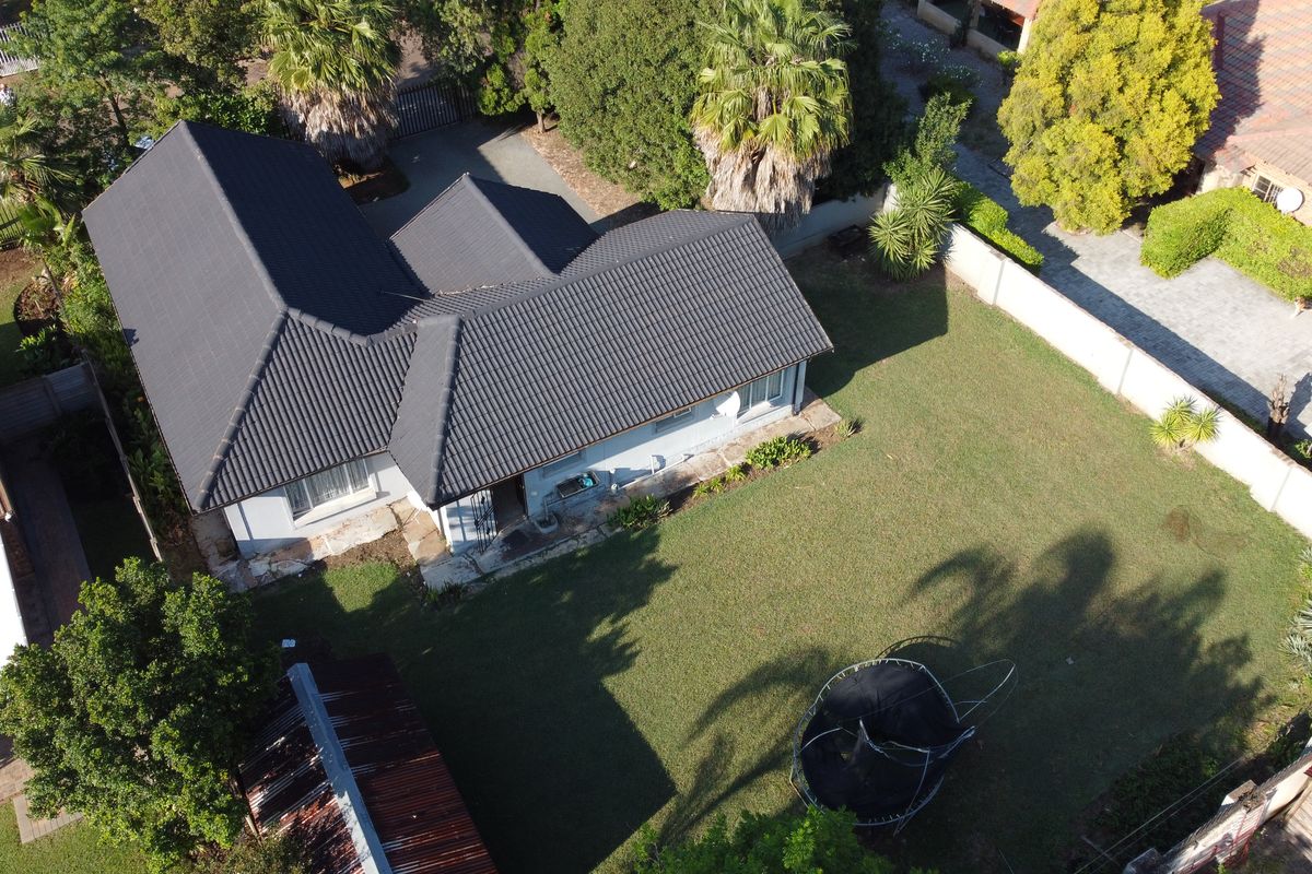 Aerial view of the property showing the house with a dark tiled roof, surrounding garden, and perimeter walling.