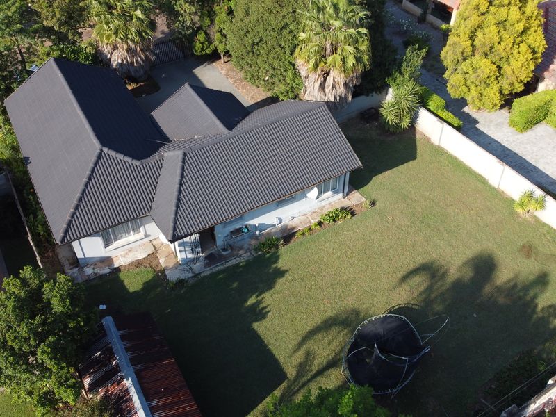 Aerial view of the property showing the house with a dark tiled roof, surrounding garden, and perimeter walling.