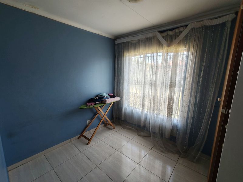 A simple bedroom featuring tiled flooring and a large window with security bars, currently used as a utility space.