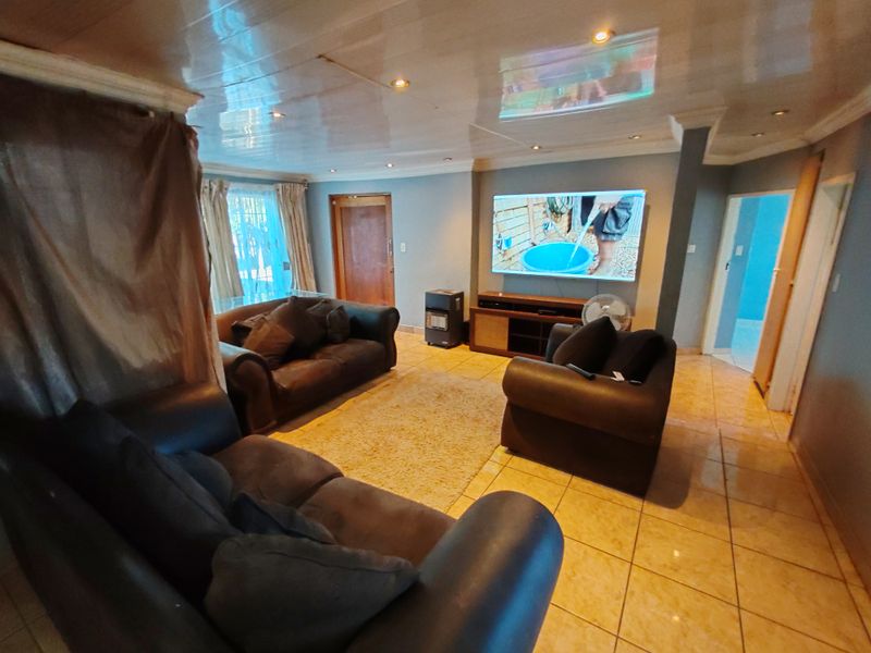 A spacious living room featuring tiled flooring, recessed downlighting, and a glossy ceiling finish, providing a functional and comfortable family living area.
