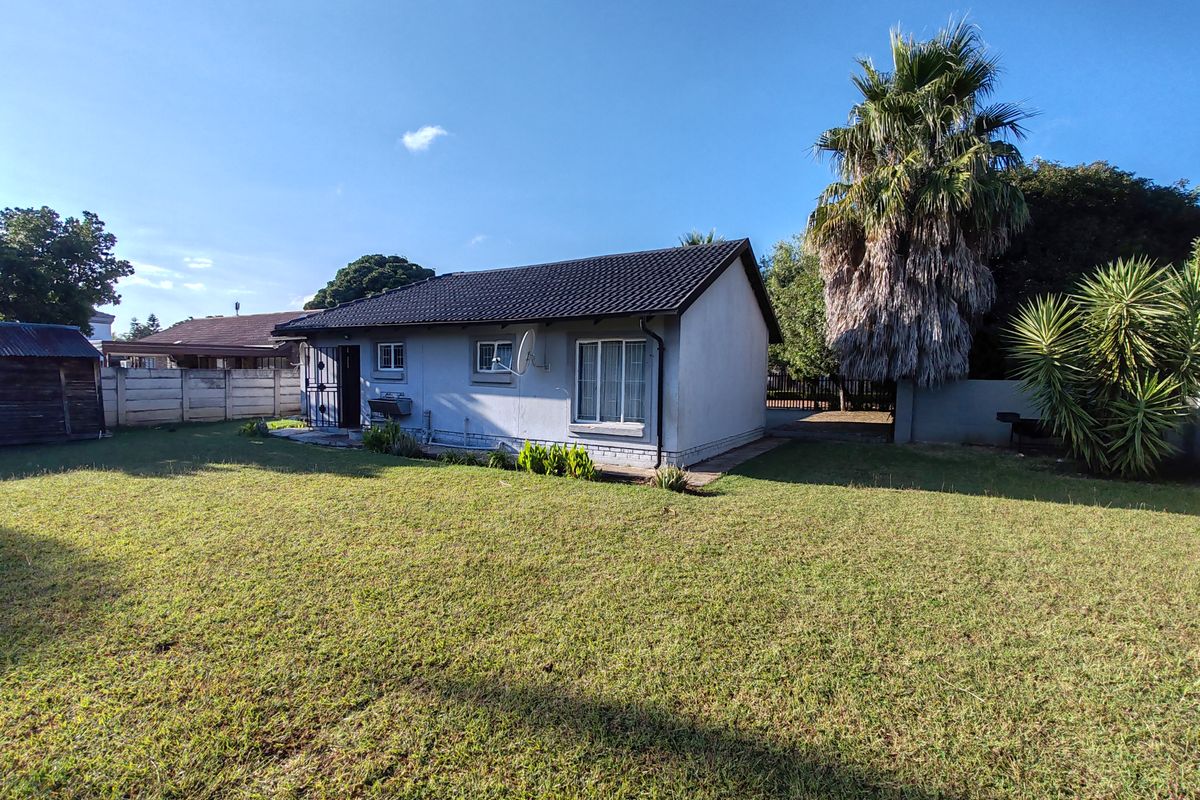 Rear view of the house featuring a tiled roof, security gate, and a spacious lawn area enclosed by a concrete perimeter wall.