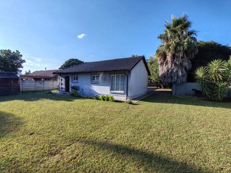 Rear view of the house featuring a tiled roof, security gate, and a spacious lawn area enclosed by a concrete perimeter wall.