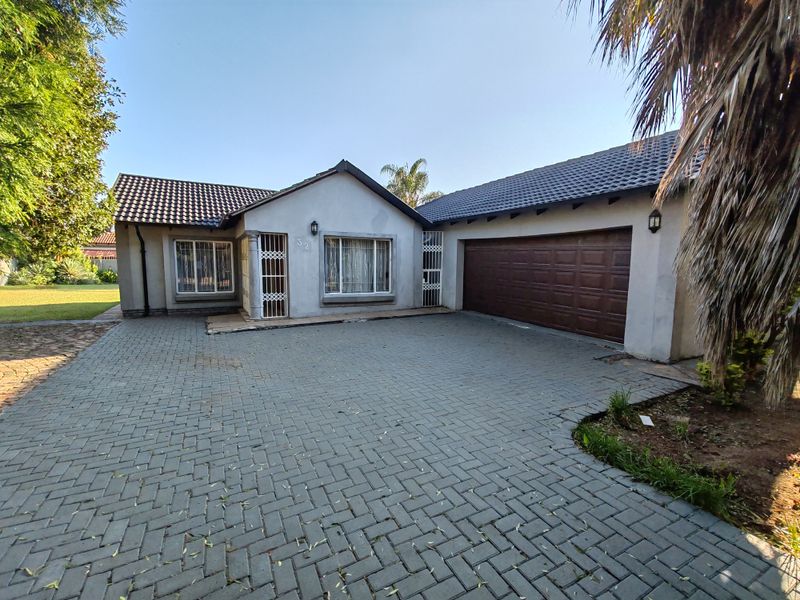 Front view of a single-story house featuring a paved driveway, double garage, and tiled roof with security gates at the entrance.