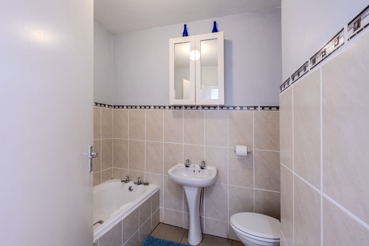 A functional bathroom featuring a bathtub, pedestal basin, toilet, and wall-mounted medicine cabinet with neutral tiled walls and flooring.
