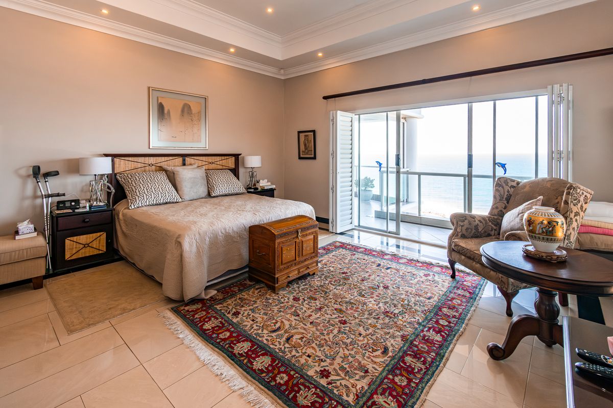 Spacious bedroom featuring a tray ceiling, recessed lighting, tiled floors, and large sliding glass doors opening onto a balcony with ocean views.