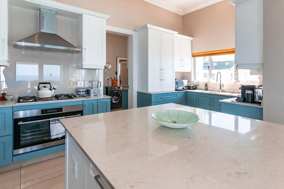 Modern kitchen featuring a central island, stone countertops, two-tone cabinetry, stainless steel appliances, and a gas hob, with an adjacent laundry area visible.