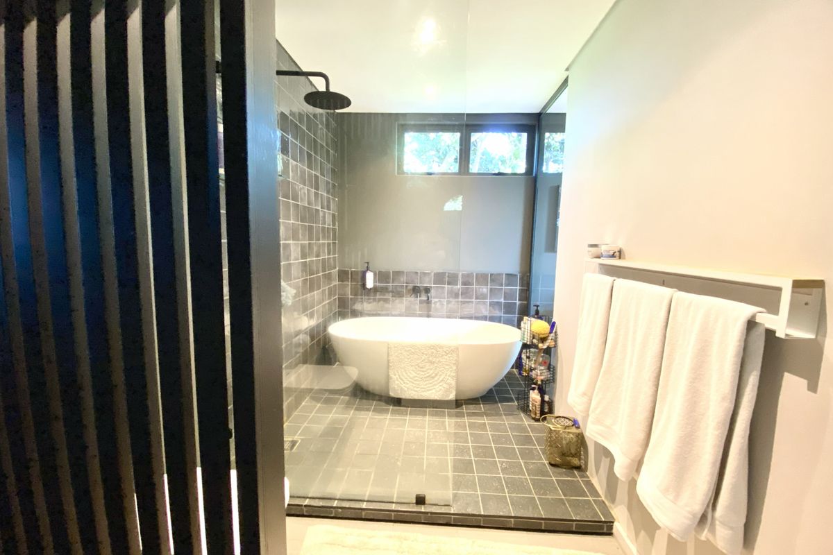 Modern bathroom featuring a freestanding bathtub, a walk-in shower with a rainfall showerhead, and dark tiled flooring.