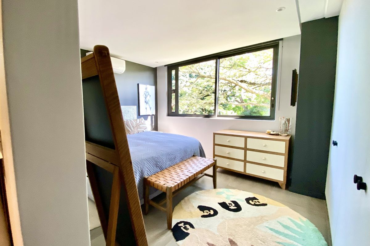 A well-lit bedroom featuring large windows with garden views, neutral flooring, and a modern split-system air conditioning unit.