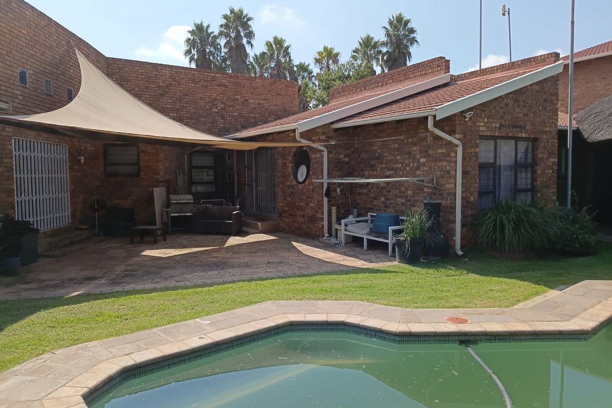 Rear exterior view featuring a brick house, paved patio area with a shade sail, and a swimming pool.