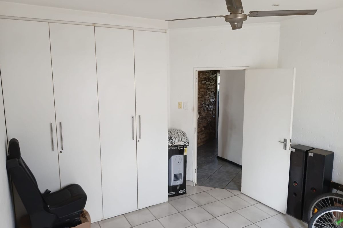 A bedroom featuring built-in cupboards, tiled flooring, and a ceiling fan, offering a clean and functional space.