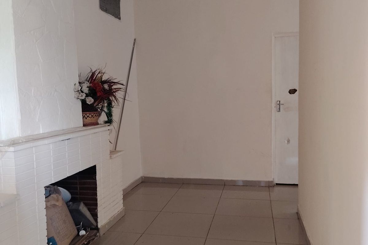 An empty living room featuring a white brick fireplace, tiled flooring, and decorative ceiling cornicing, offering a blank canvas for renovation.