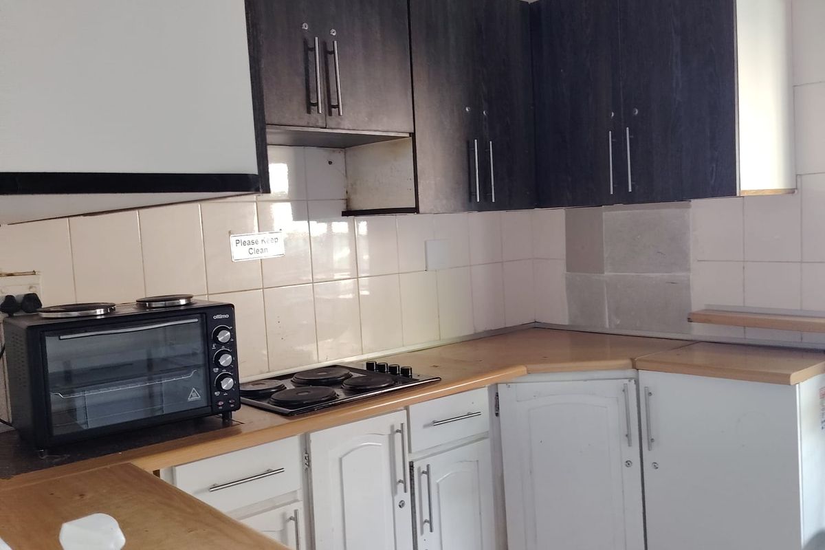A functional kitchen featuring built-in cabinetry, laminate countertops, and a tiled backsplash, currently showing signs of wear and requiring maintenance.