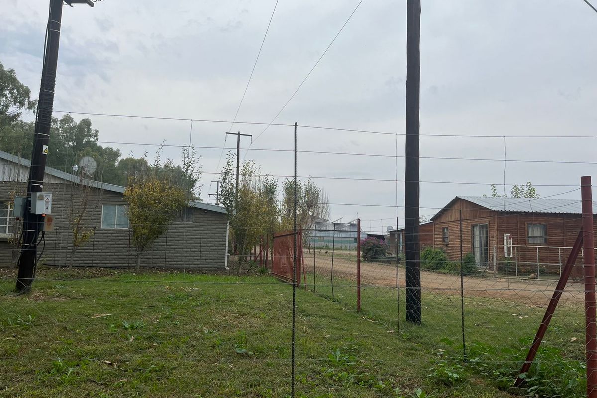 A view of the farm property grounds featuring multiple outbuildings, utility poles, and perimeter fencing on a rural landscape.