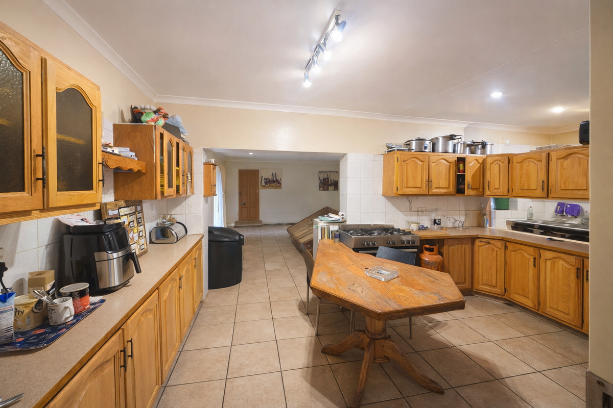 A spacious kitchen featuring traditional wooden cabinetry, tiled flooring, and a built-in gas stove, offering a functional layout with ample counter space.