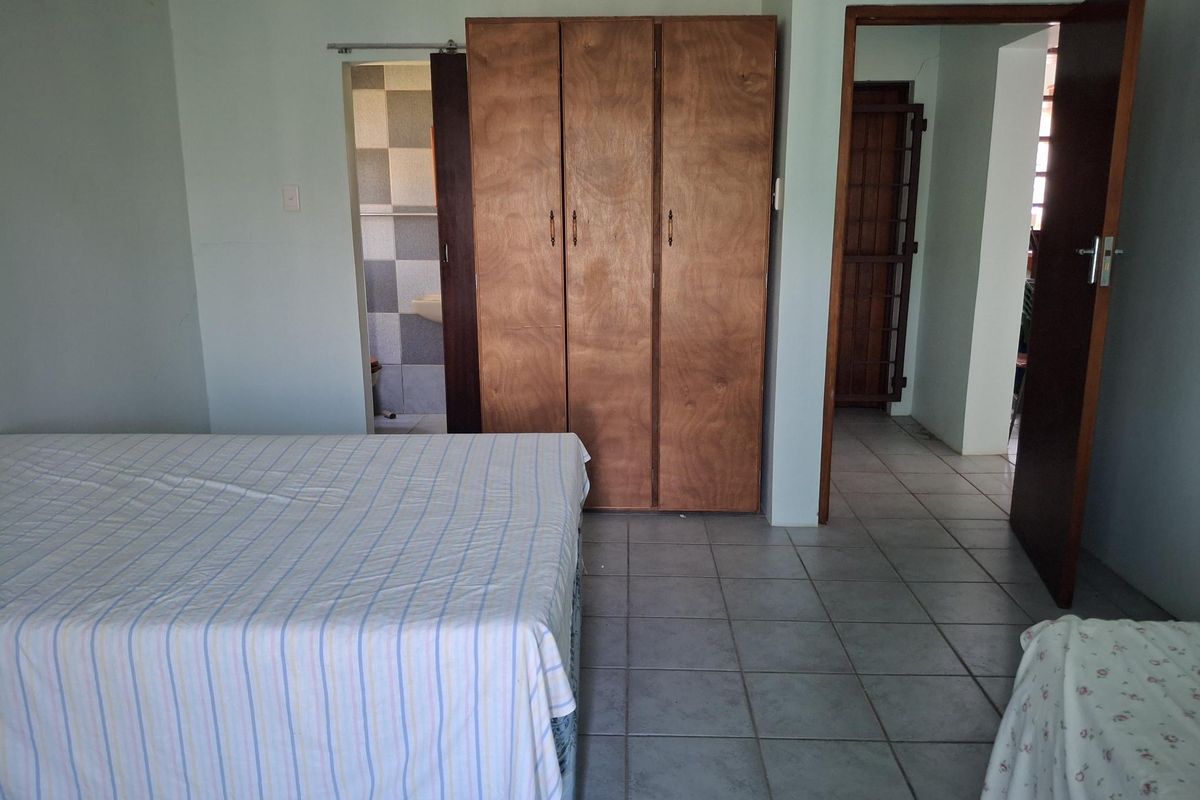 A bedroom featuring built-in wooden cupboards, tiled flooring, and direct access to an en-suite bathroom.