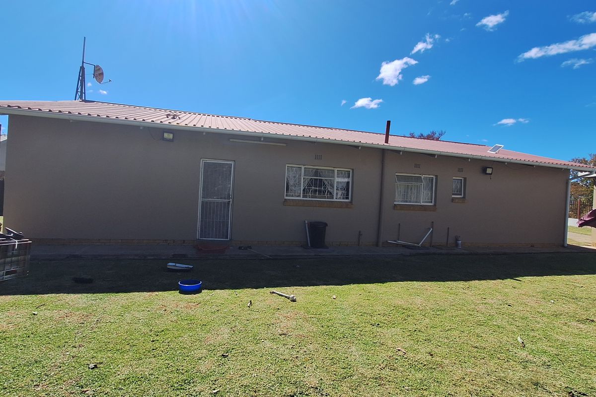 Rear exterior view of the house featuring a metal roof, security screen door, and windows overlooking a spacious backyard.