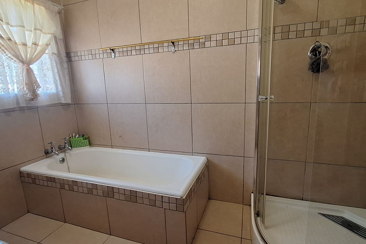 A functional bathroom featuring a built-in bathtub with tiled surround, a separate glass-enclosed corner shower, and neutral wall and floor tiling.