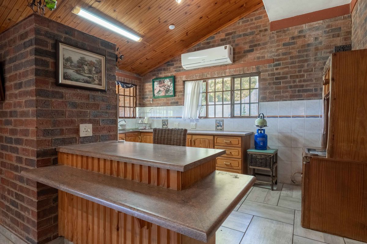 Rustic kitchen featuring exposed brick walls, timber-clad vaulted ceilings, built-in timber cabinetry, and a breakfast bar, offering a warm, traditional aesthetic.