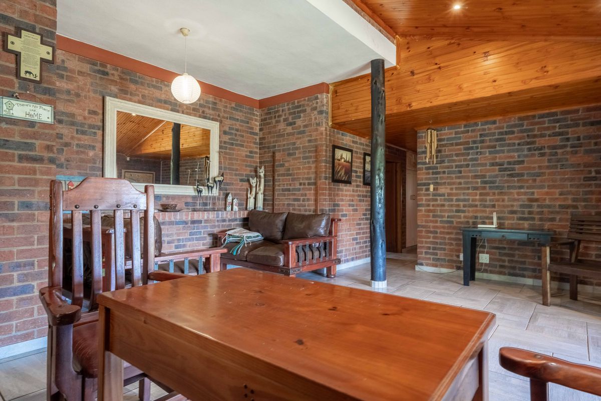 Spacious living area featuring rustic exposed brick walls, a high timber-clad vaulted ceiling, and tiled flooring with a central structural timber column.